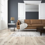 A room with light neutral hardwood flooring and a light gray area rug