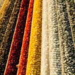 Colorful samples of carpet, layered on top of eachother. There are shades of yellow, red, cream, brown, and green.