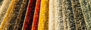 Colorful samples of carpet, layered on top of eachother. There are shades of yellow, red, cream, brown, and green.