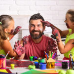 Two girls finger painting on their dads face