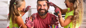 Two girls finger painting on their dads face