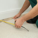 Worker with measuring tape installing new carpet indoors
