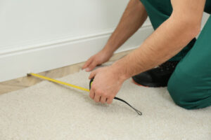 Worker with measuring tape installing new carpet indoors