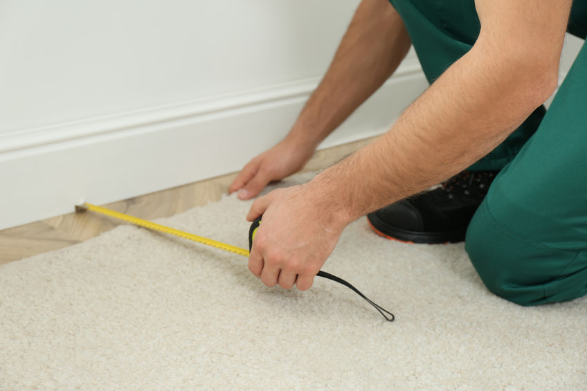 Worker with measuring tape installing new carpet indoors